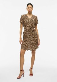 Klänning i leopardmönster med korta ärmar, V-ringning, smal midja, knä-längd, tillverkad av lätt material, parat med röda klacksandaler.