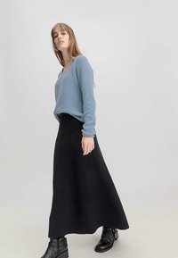Suéter de punto acanalado azul claro con escote en V, combinado con una falda maxi acanalada negra. Botas negras de tobillo completan el look.