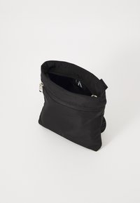 Sac en nylon noir avec une fermeture éclair, texture douce et une petite boucle en tissu. Présente un design simple et épuré avec un minimum de détails.