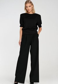 Czarny krótki top z okrągłym dekoltem, zestawiony z wysokimi spodniami czarnymi o szerokich nogawkach. Tkanina wydaje się gładka, z minimalną teksturą.