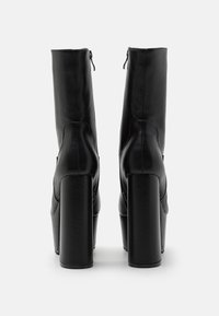 Bottes à plateforme noires à la cheville, en cuir texturé, talons carrés et fermeture éclair à l'arrière. Des coutures décoratives sont également visibles.