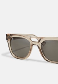 Ochelari de soare Ray-Ban cu o ramă maro translucidă, lentile gri, formă angulară și detaliu decupat în partea superioară a ramei.
