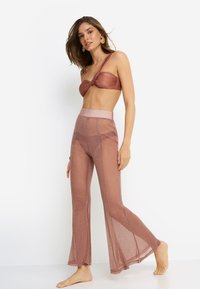 Μεταλλικό τοπάκι bandeau σε ροζ χρυσό με στριφτό σχέδιο, συνδυασμένο με διάφανο, καμπάνα παντελόνι. Και τα δύο έχουν λαμπερή υφή και ψηλή μέση.