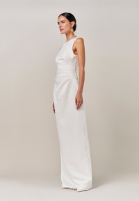 Vit ärmlös satinklänning med åtsittande överdel och draperade detaljer vid midjan, som faller till golvet. Mjuk textur och minimalistisk design.