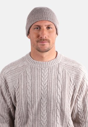 Bonnet côtelé beige et pull en grosse maille torsadée. Le pull présente des motifs texturés et un col rond. Les matériaux doux procurent de la chaleur.