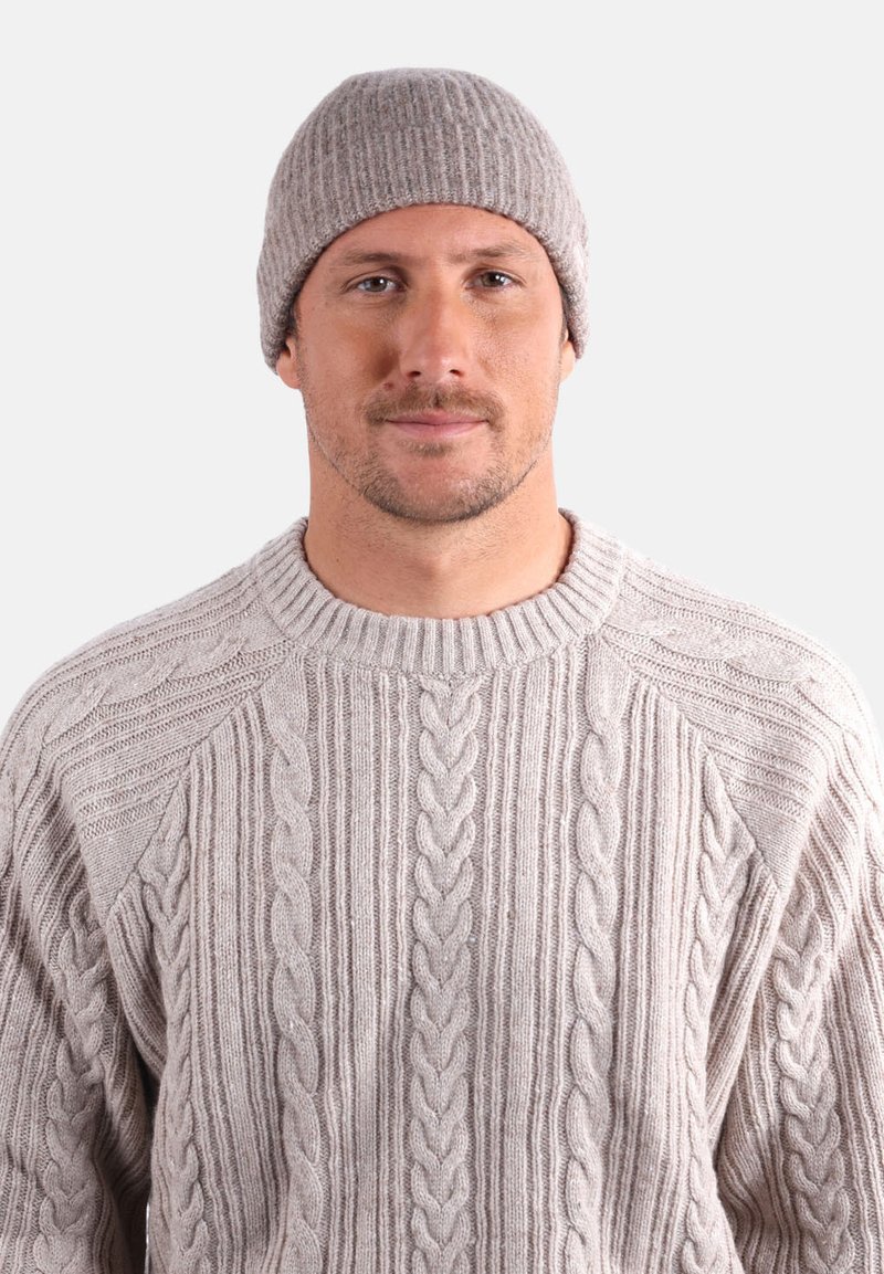 Bonnet côtelé beige et pull en grosse maille torsadée. Le pull présente des motifs texturés et un col rond. Les matériaux doux procurent de la chaleur.