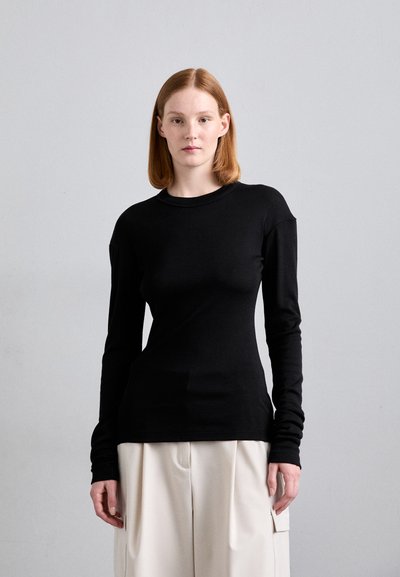 Haut noir à manches longues avec un col rond, présentant une silhouette ajustée et des épaules sans couture, fabriqué dans un tissu lisse et extensible.