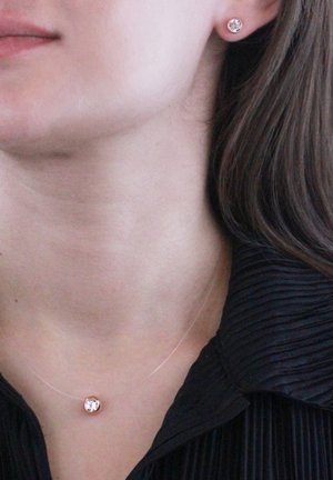 Collana in oro rosa con una pietra centrale trasparente, abbinata a orecchini a bottone coordinati. La collana ha una catena sottile e un design minimalista.