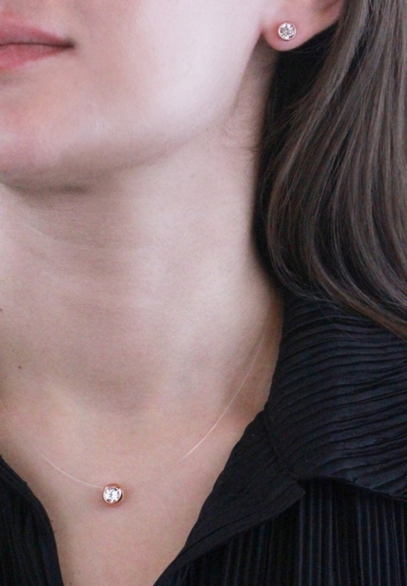 Collana in oro rosa con una pietra centrale trasparente, abbinata a orecchini a bottone coordinati. La collana ha una catena sottile e un design minimalista.