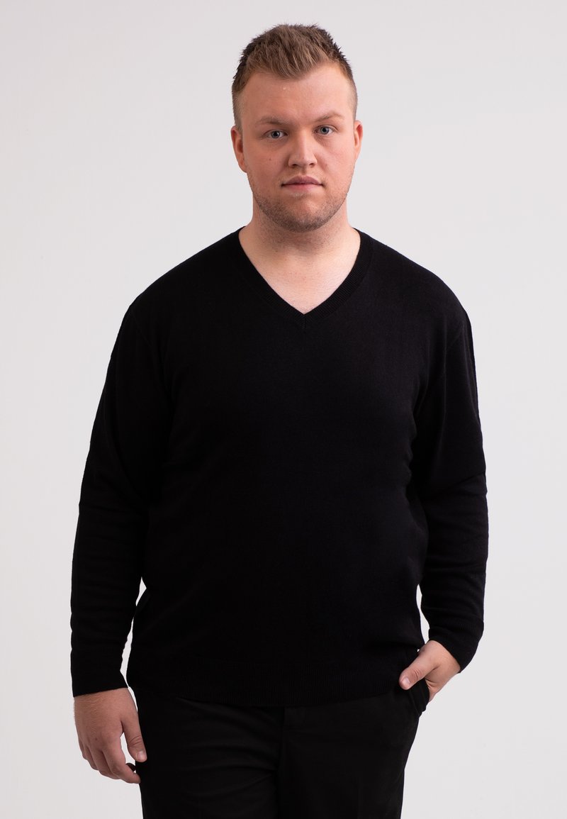 Svart v-ringad tröja i mjukt material med långa ärmar och en figurnära design. Modell står mot en neutral bakgrund.