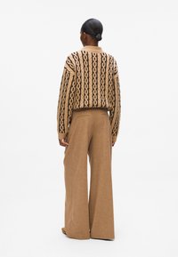 Strikkegenser med mønsterdesign i beige og svart, kombinert med brede beige bukser som viser en jevn tekstur og avslappet passform.