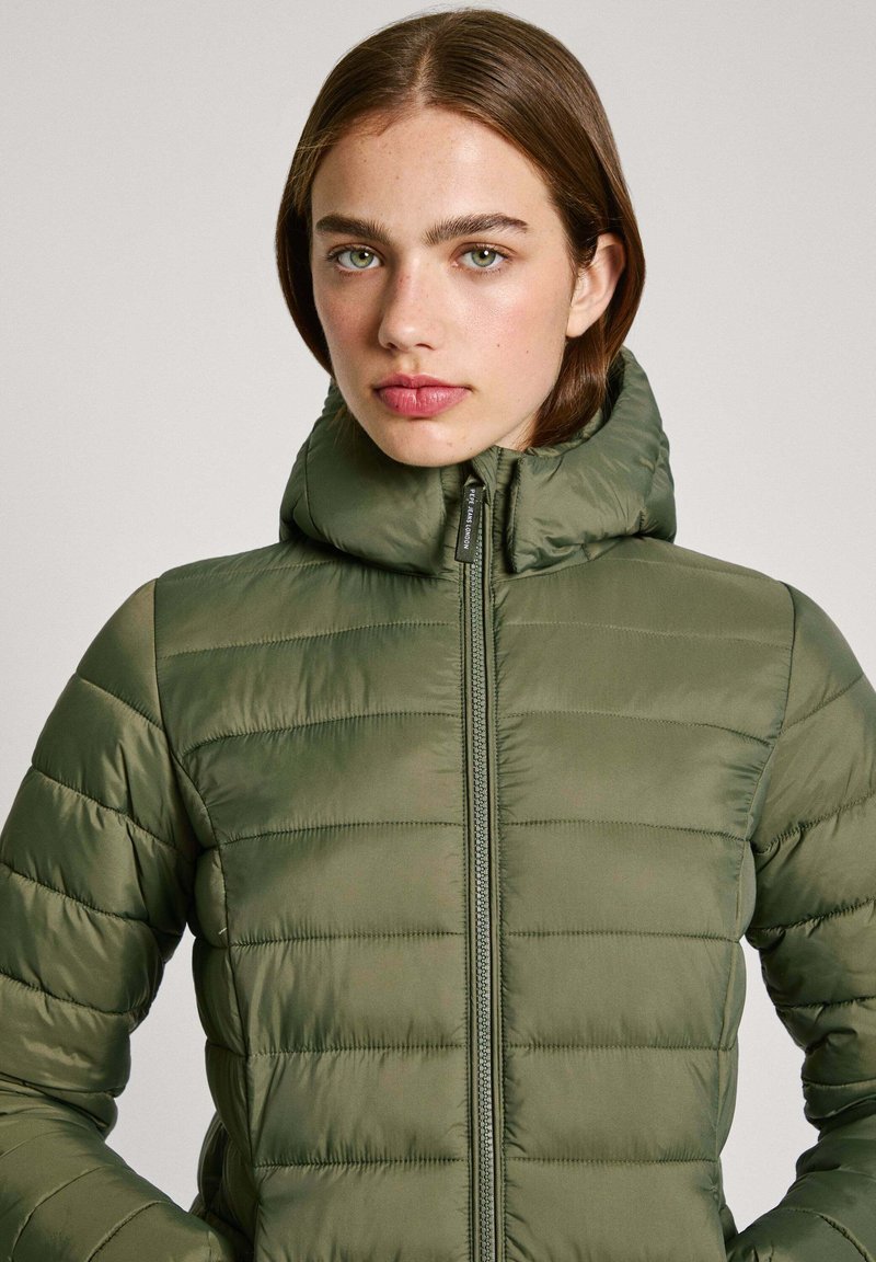 Chaqueta acolchada verde con patrón de acolchado horizontal, cuello alto, cierre con cremallera y bolsillos laterales; presenta una textura lisa y brillante.
