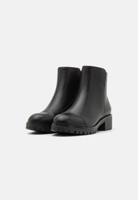 Bottines en cuir noir avec un bout rond, un léger talon et une semelle en caoutchouc texturé. Elles présentent une finition lisse et une fermeture éclair latérale pour un enfilage facile.