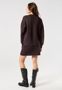 Ciemnofioletowy, błyszczący sweter z dzianiny i pasująca spódnica, noszone z wysokimi czarnymi skórzanymi butami na kolana z akcentami w postaci klamr.