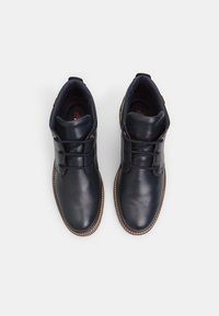 Botine din piele bleu marin, cu o textură netedă, vârf rotund, design cu sireturi și cusături de contrast pe talpa maro.
