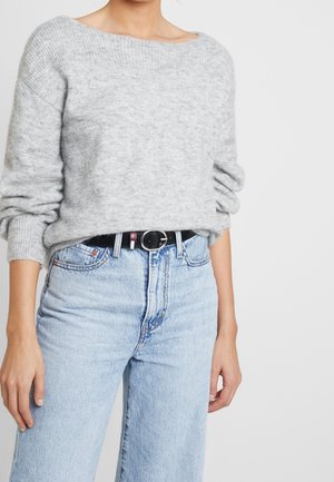 Personne portant un pull en maille gris clair rentré dans un jean bleu clair taille haute avec une ceinture noire et une boucle argentée.