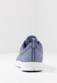 Lilla mesh-sportsko med tekstureret yderside, hvid sål og en kontrasterende grå detalje på siden. Set bagfra.