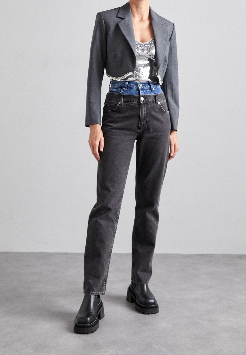 Blazer gris sobre una blusa de lentejuelas, combinado con jeans negros de tiro alto y botas de plataforma gruesa negras. Diseño y materiales simples y estructurados.