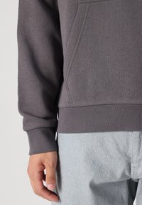 Grijze sweatshirt met een geribde zoom en manchetten, met een voorkantzak en een zachte textuur. Gecombineerd met lichtblauwe denim broek.