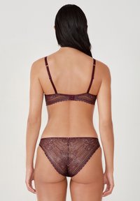 Reggiseno in pizzo e perizoma abbinato in un profondo bordeaux. Caratterizzato da spalline regolabili, bordi ondulati e motivi floreali con una texture semi-trasparente.