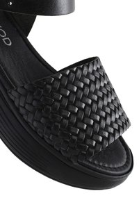 Sandalo con tacco nero, dotato di tomaia in pelle intrecciata, soletta in pelle liscia e suola piatta texturizzata. Inclusa una cinghia regolabile per la caviglia.