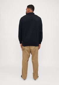 Schwarzer Pullover mit Kragen, strukturiertem Stoff und geripptem Saum. Kombiniert mit beigen Cargo-Hosen, die seitliche Taschen und einen lockeren Schnitt haben.