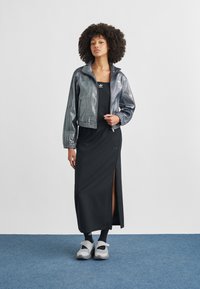 Srebrna metalik jakna na patentni zatvarač, crna haljina bez rukava s bočnim prorezom i siva obuća. Jednostavan dizajn s vidljivim logotipima brenda.