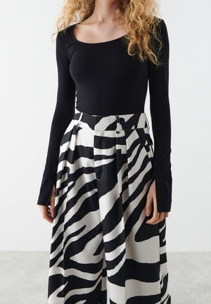 Kvinde iført en tætsiddende sort langærmet top og højtaljede vidde bukser med dristige sort-hvide zebra-striber.