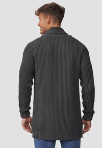 Cardigan lungo in grigio carbone, realizzato in maglia con un motivo testurizzato, polsini e orlo a costine. Presenta un colletto a scialle e arriva fino a metà coscia.