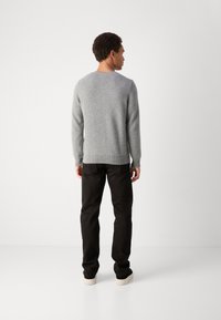 Pilkas megztinis su ilgomis rankovėmis, apvaliu kaklu ir elastiniais rankogaliais. Derinamas su juodomis kelnėmis ir batais su šviesiomis padais. Paprastas, tekstūruotas dizainas.