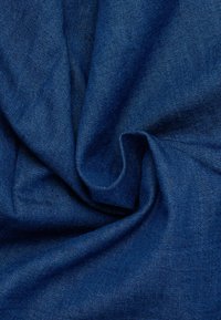 Donkerblauwe denim stof met een zachte, gestructureerde oppervlakte, voorzien van een geweven patroon en gedrapeerde plooien die diepte en beweging creëren.