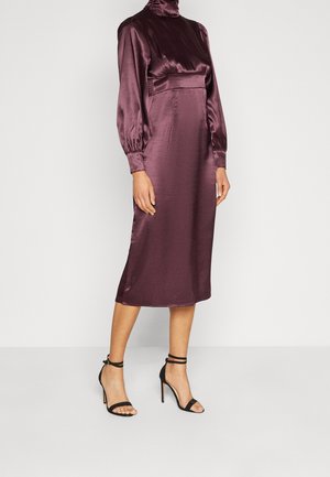 Vestido midi de satén púrpura con cuello alto y mangas abullonadas, que presenta un corsé entallado y una textura suave, combinado con tacones negros con tiras.