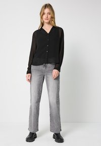 Camisa negra transparente con botón y cuello, combinada con jeans acampanados gris claro y botas negras de plataforma. Diseño sencillo, moderno y de corte relajado.