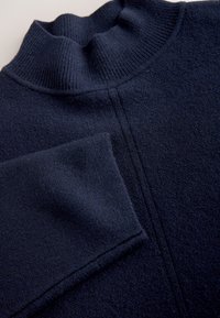 Dark navy blue wool sweater with a high ribbed collar and visible seam running vertically along the front.