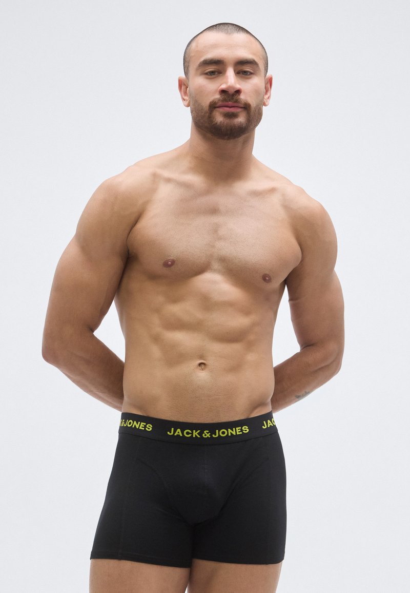 Boxers noirs avec une ceinture élastique jaune affichant la marque « JACK & JONES » ; le mannequin, de carrure musclée, est debout les bras derrière le dos.