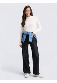 Maglia bianca a maniche lunghe, pantaloni larghi in denim scuro, maglione azzurro chiaro annodato in vita e sneakers bianche. Tessuto liscio e vestibilità comoda.