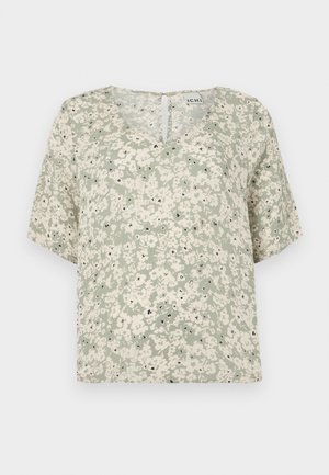 Kortermet bluse i lysegrønn stoff med hvite blomster mønster og svarte detaljer. V-hals med en liten nykelhulldetalj bak.