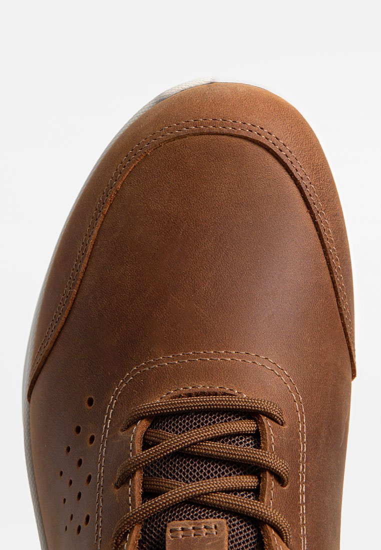 Brauner Lederschuh mit glatter Oberfläche, runder Zehenpartie und kontrastierendem dunklem Mesh-Zungenbereich. Verfügt über braune Schnürsenkel und durchbrochene Details an der Seite.