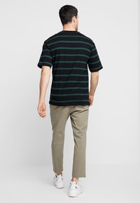 T-shirt nera a maniche corte con strisce orizzontali verdi, abbinata a pantaloni tapered khaki e sneakers bianche.