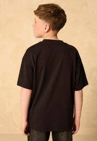Tricou din bumbac negru, cu mâneci scurte. Prezintă un gât rotund clasic. Textură netedă, fără modele sau accente vizibile.