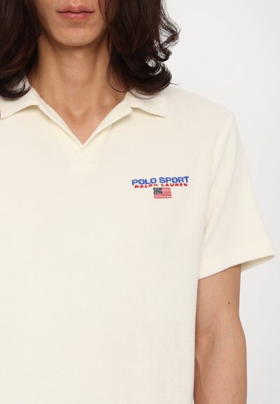Korte mouw crèmekleurige polo met een zachte textuur. Voorzien van "POLO SPORT" geborduurd in blauw en rood met een klein Amerikaans vlagpictogram.