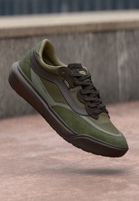 Green athletic sneaker with a mix of textured materials. Features brown accents, a padded collar, and a gripping rubber sole.