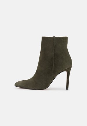 Olivenfarvet ruskindsankelstøvle med spids tå, hælhøjde på cirka 10 cm og en glat, højglanssål.