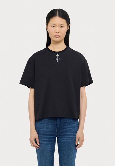 Sort oversized t-shirt lavet af blød bomuld, med korte ærmer og et lille detaljeret sølv grafik på brystet. Casual pasform.