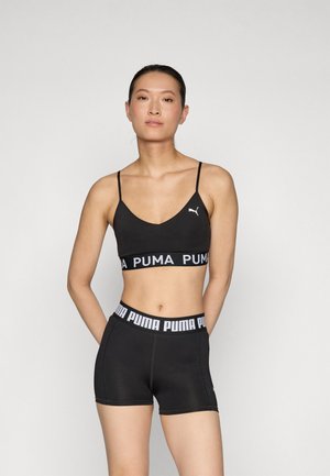 Black sports bra with thin straps and a PUMA logo, paired with black shorts featuring a logoed waistband. Smooth texture, form-fitting design.