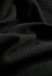 Material textil negru cu o textură striată, prezentând pliuri moi, suprapuse și o strălucire subtilă care evidențiază materialul său durabil.