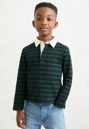 Koszulka polo w paski z długim rękawem w ciemnozielonym i granatowym kolorze, z białym kołnierzykiem i listwą z guzikami. Noszona z jasnoniebieskimi jeansami.