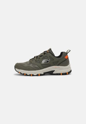 Zapatilla deportiva verde con parte superior de malla texturizada, acentos naranjas y una suela gruesa y texturizada con mayor agarre para la tracción.