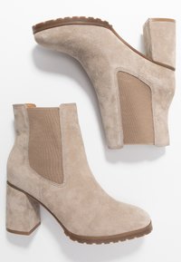 Botines de ante beige con paneles laterales elásticos, tacones de bloque y suelas de goma texturizadas. Presentan puntera redondeada y detalles de costura.