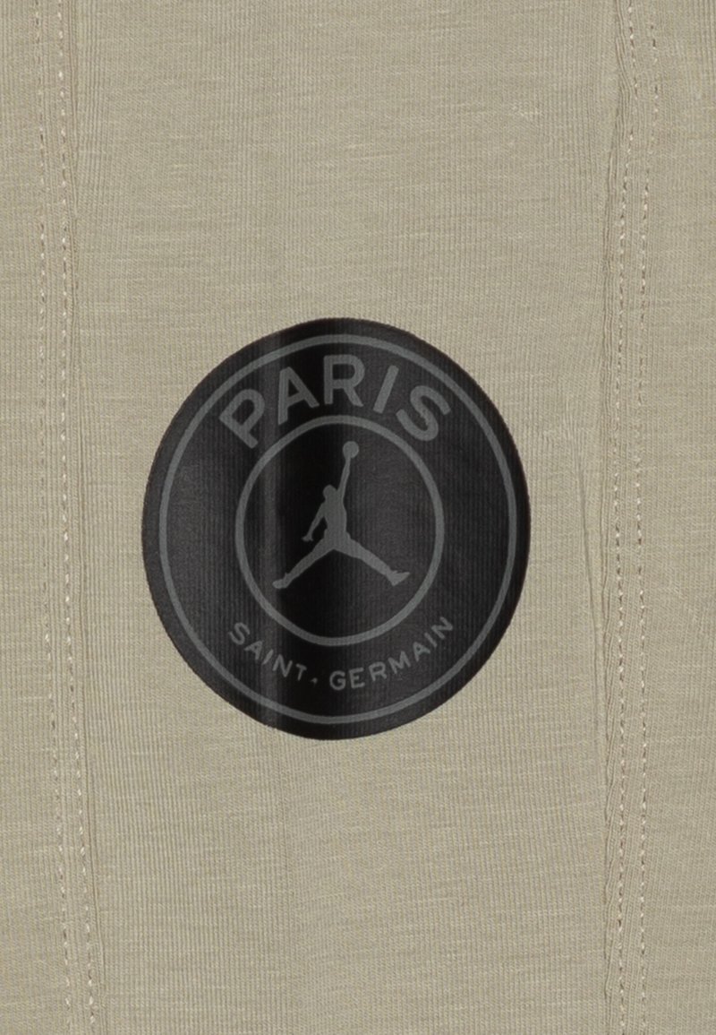 Beżowa tkanina o żebrowej fakturze z dużym czarnym okrągłym logo z napisem "PARIS" i "SAINT-GERMAIN" oraz sylwetką w centrum.